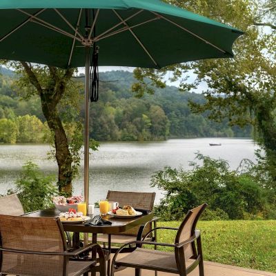 Outdoor dining setup with a lake view, green umbrella, chairs, and a boat in the distance.