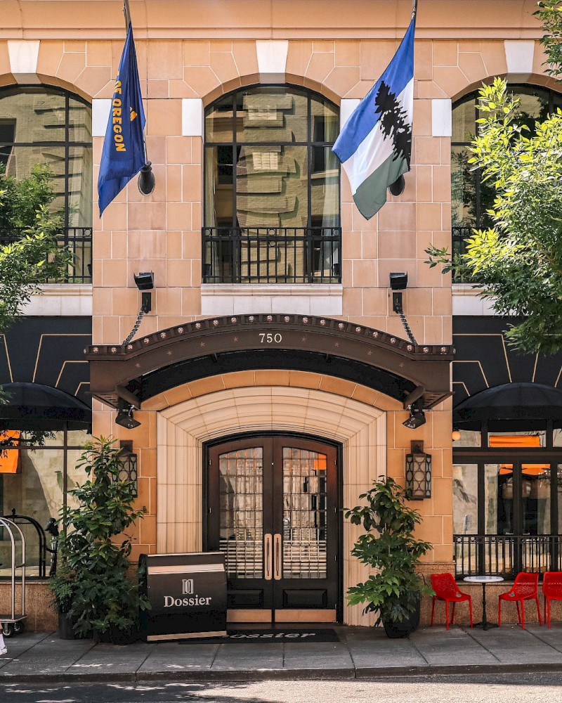 The image shows a building with flags, trees, and a person walking past, featuring a sign that reads 