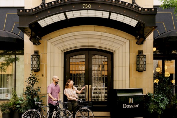 Two people with bikes outside a building named Dossier.
