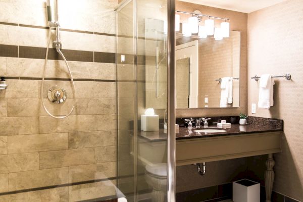 The image shows a modern bathroom with a glass enclosed shower, a sink with a granite countertop, a large mirror, and towel racks.