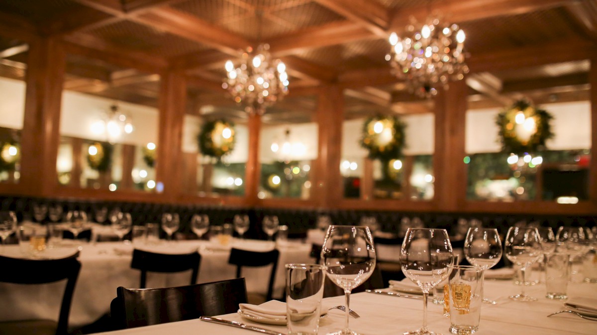 A beautifully decorated restaurant with chandeliers, white tablecloths, and neatly arranged wine glasses, ready for an elegant dinner setting.