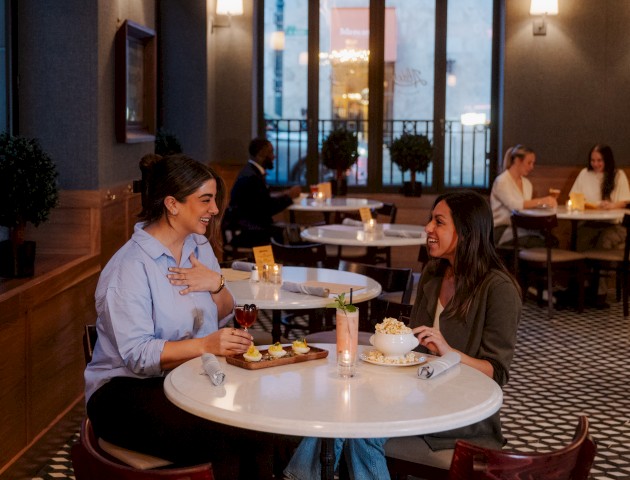 A cozy restaurant scene with dim lighting, couple of tables, wine glasses, and people dining in the background, creating a warm intimate vibe.