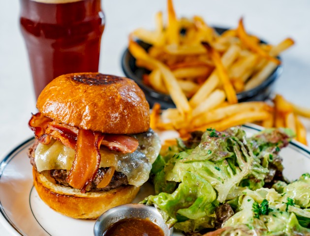 A plate with a cheeseburger, bacon, salad, fries, and a glass of beer.