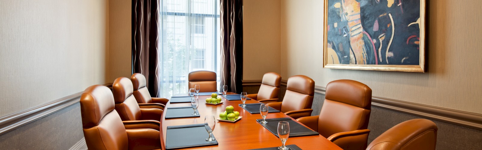 A modern conference room with a long table, leather chairs, artistic lighting, and wall art. Placements and glasses are set on the table.
