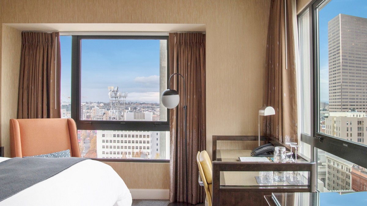 A hotel room with large windows showcasing a city skyline and tall buildings.