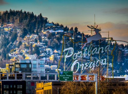 The image features a snowy hillside cityscape in Portland, Oregon, with a large neon sign of a deer above the city.