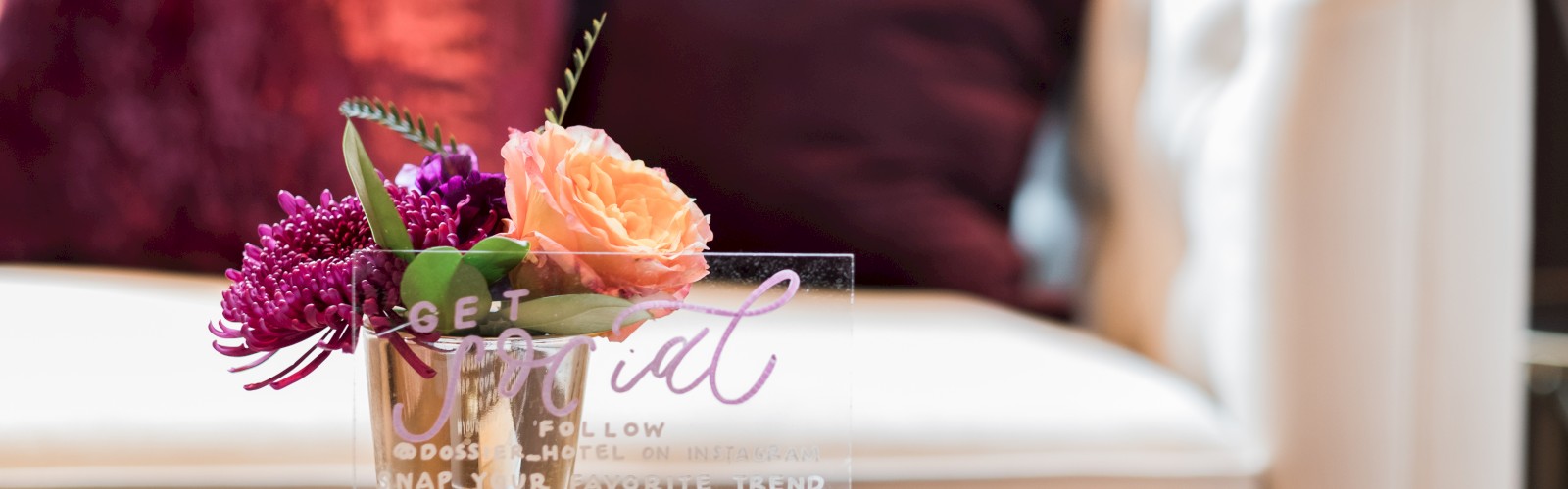 A small bouquet in a vase beside a clear sign on a table, with a white sofa and colorful pillows in the background.