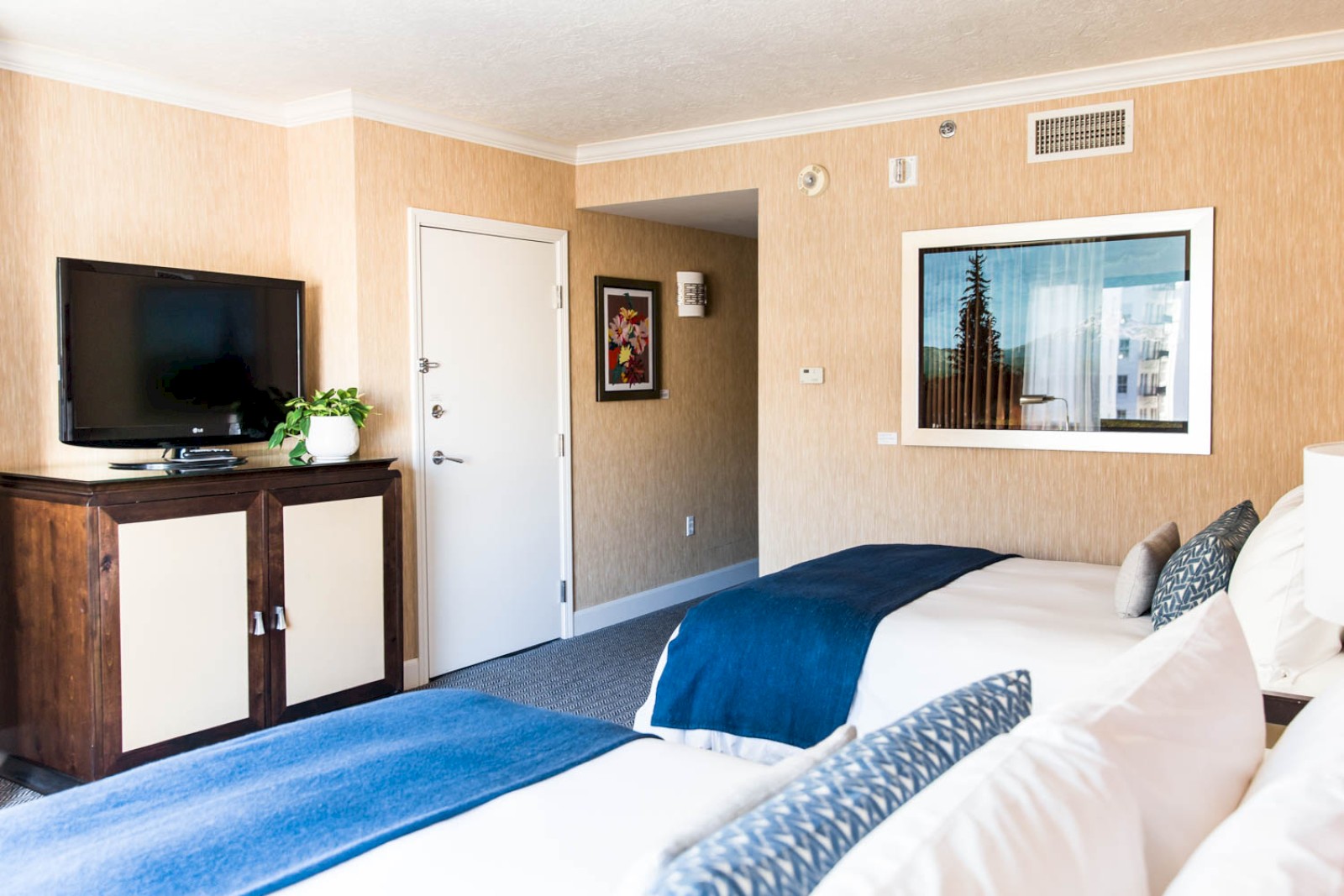This image shows a hotel room with two beds, a flat-screen TV on a wooden stand, artwork on the walls, and a door, ending the sentence.