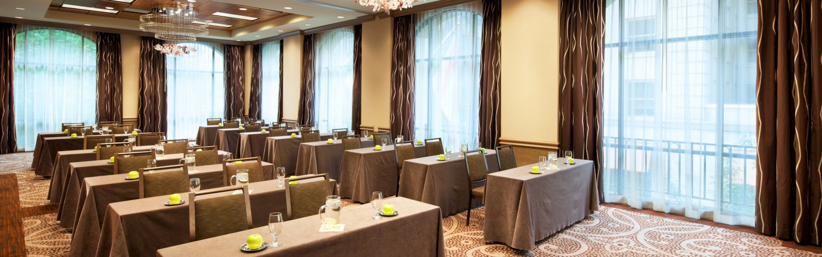 The image shows a conference room set up in a classroom style with rectangular tables, chairs, bottles of water, and notepads on each table.