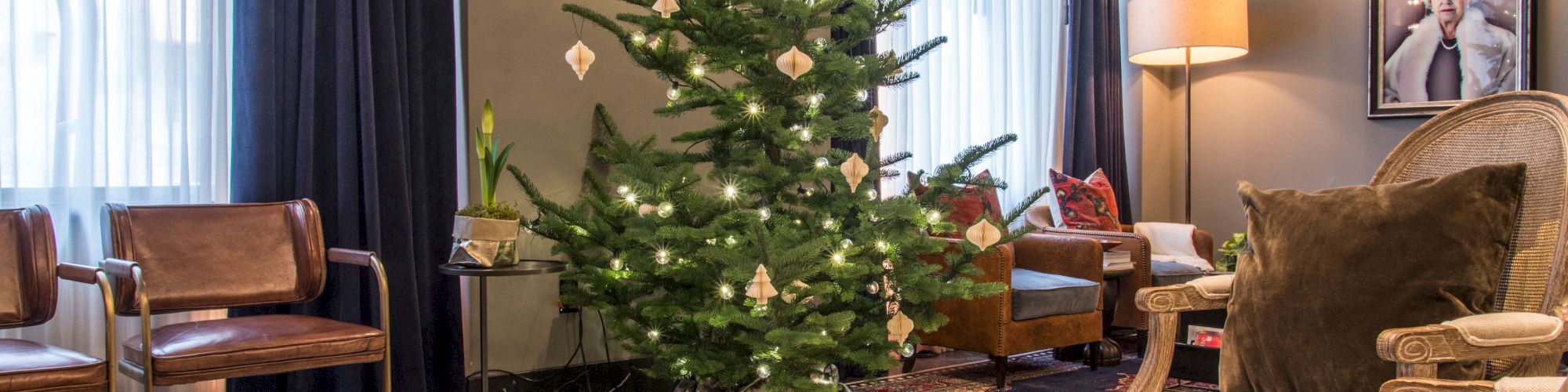 A cozy living room with a decorated Christmas tree, modern furniture, a glass coffee table, and a portrait on the wall.