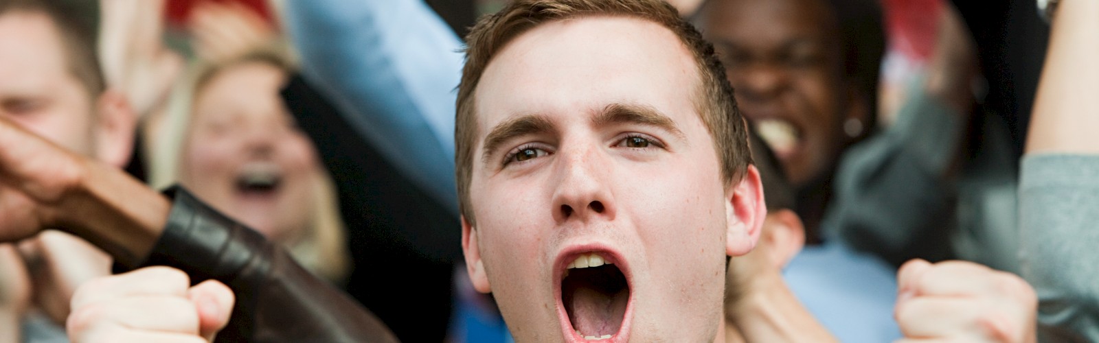 A group of people energetically cheering, with one person in the foreground expressing excitement, fists clenched and mouth open.