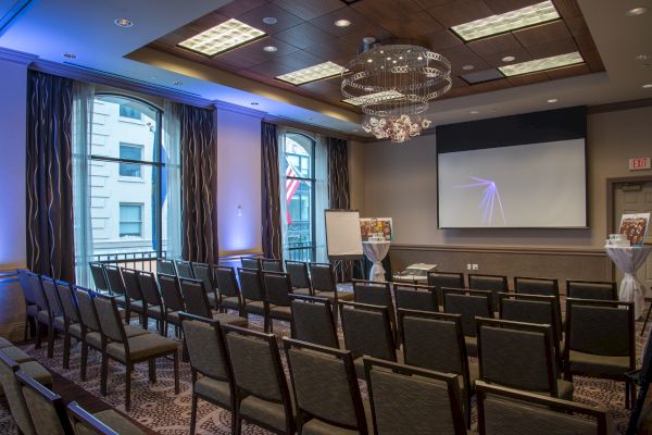 A conference room with rows of chairs, a large screen, a flipchart, and elegant lighting, set up and ready for a presentation or meeting.