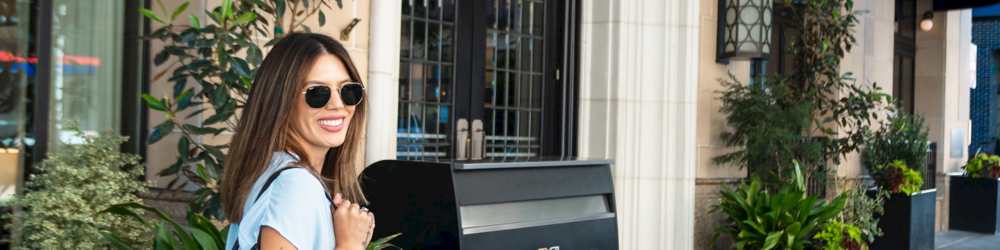 A person with sunglasses and a backpack stands outside the entrance of a building labeled 