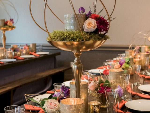 An elegant table setting with gold geometric centerpieces, candles, and floral arrangements, ideal for a formal event or celebration.