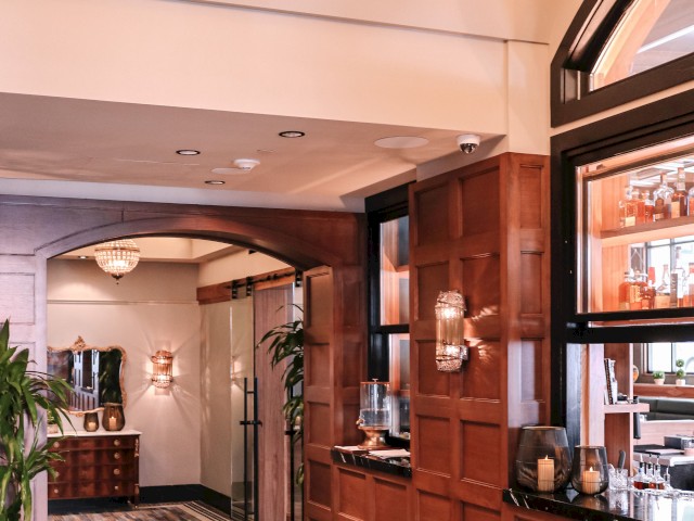 A well-lit hallway featuring wooden paneling, a glass display case, and a large archway leading to another room with a patterned floor.