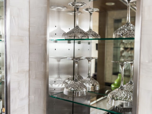 The image shows a glass cabinet with multiple shelves displaying upside-down crystal wine glasses and a reflective backdrop, ending the sentence.