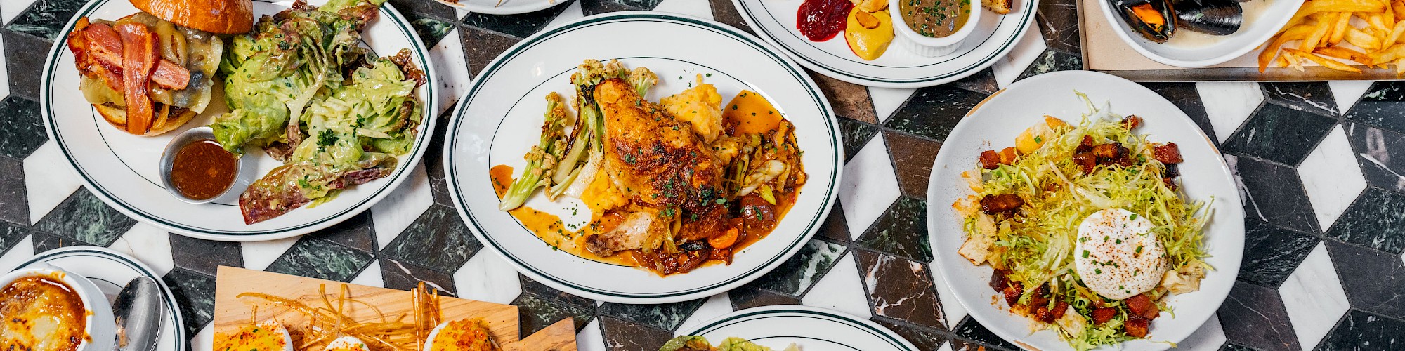 The image displays a variety of dishes on a table, including salads, seafood, steak, fries, and more, all arranged on a checkered surface.