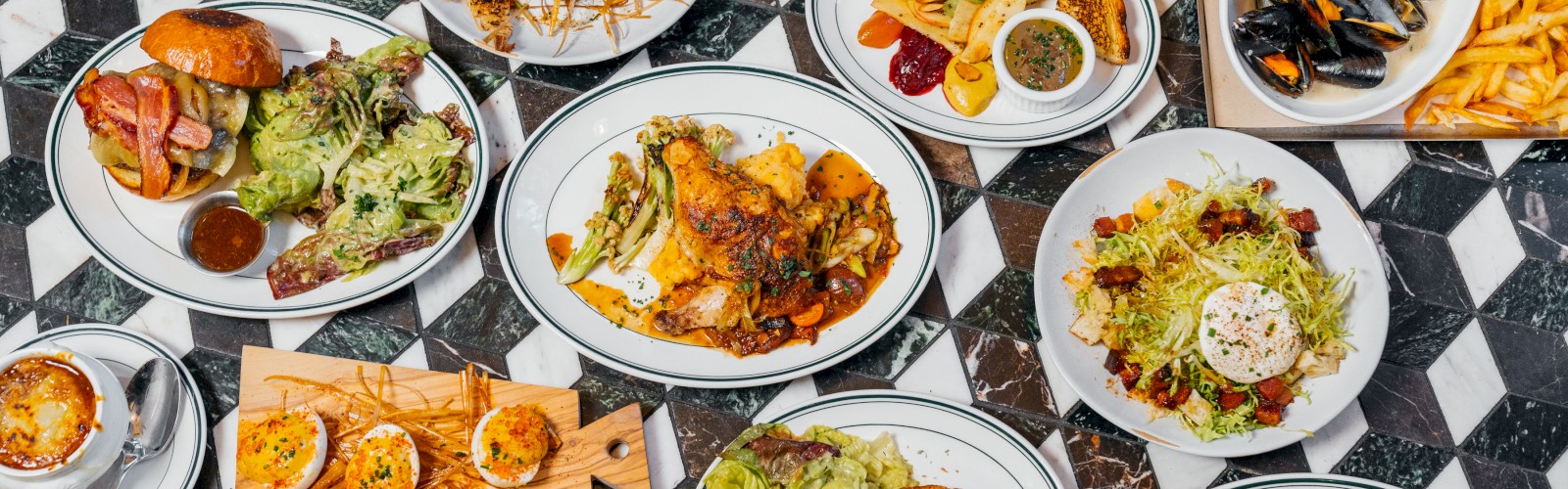 The image shows a table with various dishes including salads, steak, fries, mussels, toast, a burger, grilled vegetables, and desserts.