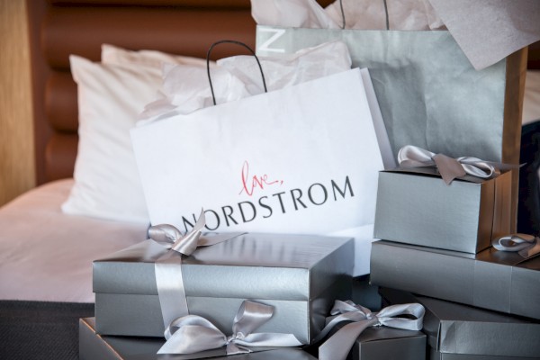 Gift boxes and a Nordstrom shopping bag are arranged on a bed, all tied with silver ribbons and tissue paper in the bags.