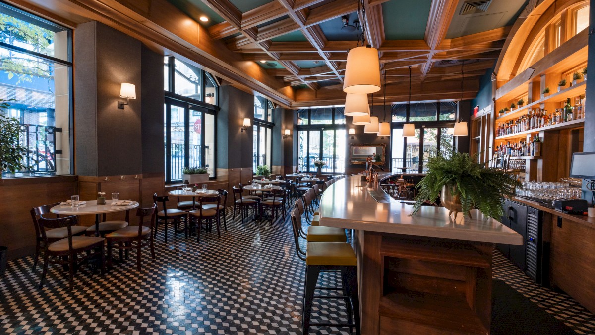 The image shows a stylish restaurant interior with tables, chairs, a bar, pendant lights, and a patterned floor, creating a cozy ambiance.