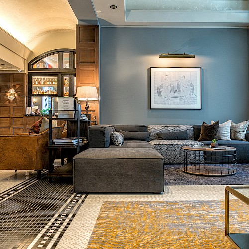 A modern living area with a gray sectional sofa, artwork on the wall, and a cozy bar in the background.