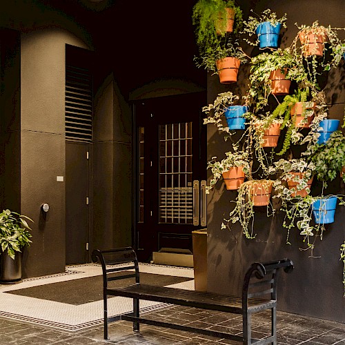 The image shows a wall with colorful potted plants, a bench, and a door, creating a cozy, inviting atmosphere.