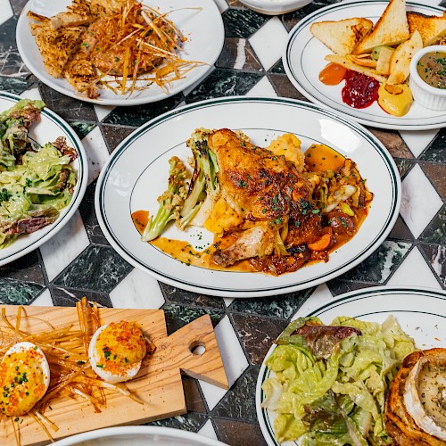 The image displays an assortment of dishes including roast chicken, deviled eggs, salads, and sandwiches on a patterned tabletop.