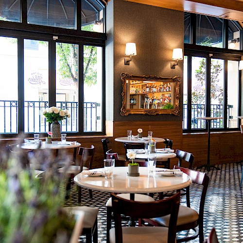 The image shows a stylish restaurant interior with neatly set tables, chairs, wall mirrors, and large windows. The floor has a checkered pattern.