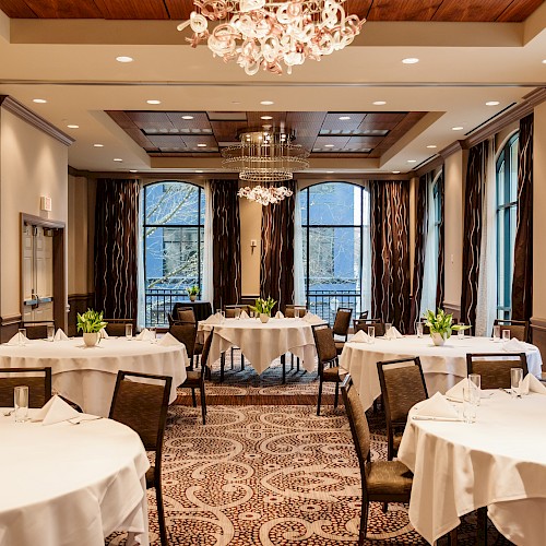 The image shows an elegantly decorated banquet hall with round tables, white tablecloths, and floral centerpieces, ready for an event.