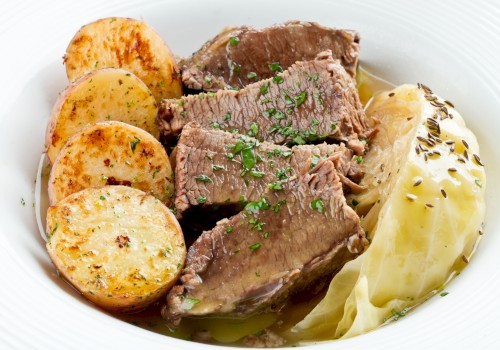 The image shows a dish with slices of cooked beef, roast potatoes, and cabbage garnished with herbs on a white plate.