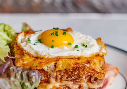 A croque madame sandwich topped with a fried egg, garnished with chives, and served with a side of greens on a plate.