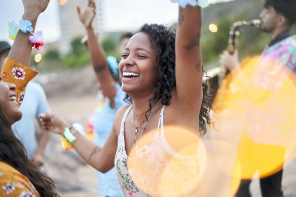 People are joyfully dancing outdoors, with a musician playing a saxophone in the background, creating a festive atmosphere.