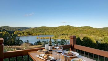 Outdoor dining set up with food on table, overlooking a scenic lake and hills.