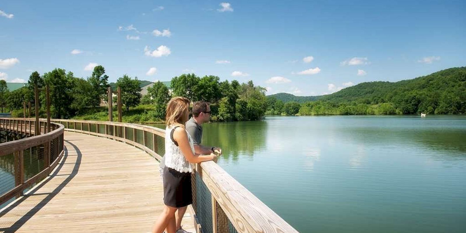 Two people are on a lakeside boardwalk enjoying the view.
