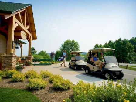 Two golf carts in front of a building, people walking, lush greenery under a blue sky.