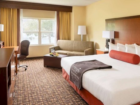 A tidy hotel room with a bed, sofa, desk, and TV.