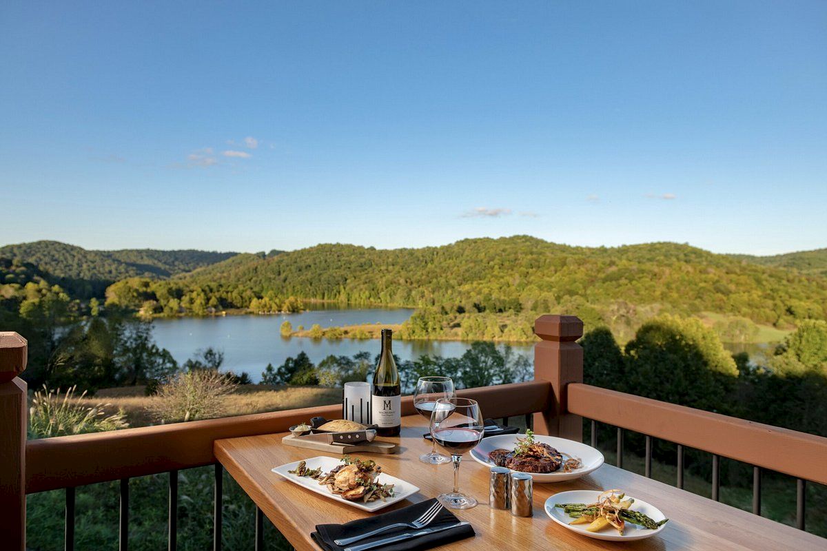 A tranquil dining setup on a deck with a serene lake view, wine, and food at sunset.