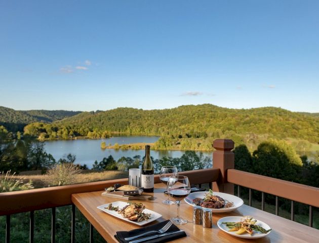 Dining setup on a deck overlooking a serene lake and hills.