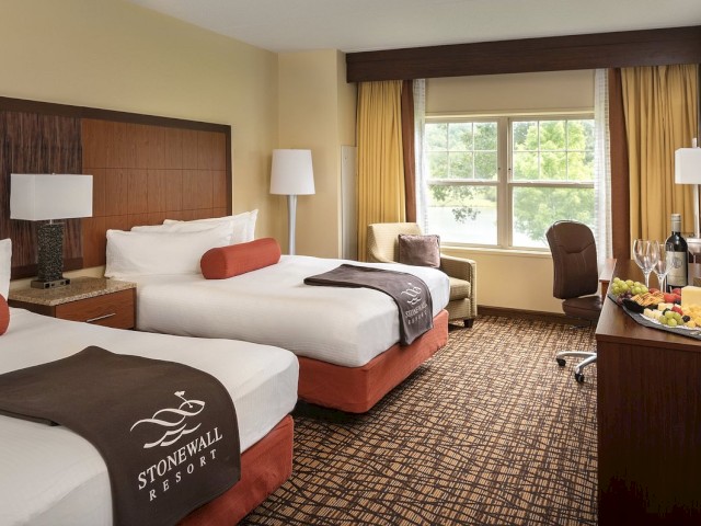 A hotel room with two beds, a side table with lamps, a desk, chair, and a food tray.