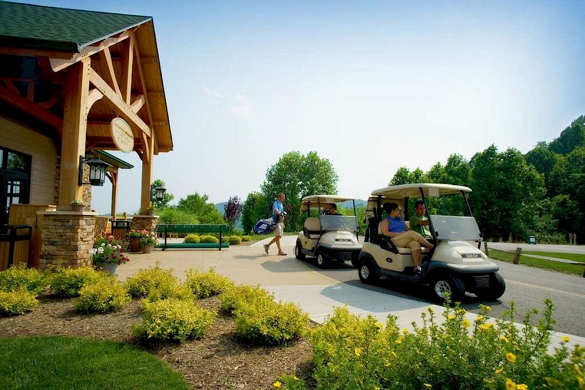 Two golf carts parked by a building with people, surrounded by greenery and a clear sky.