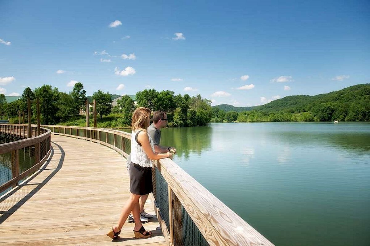 Two people are on a lakeside boardwalk enjoying the view on a sunny day.