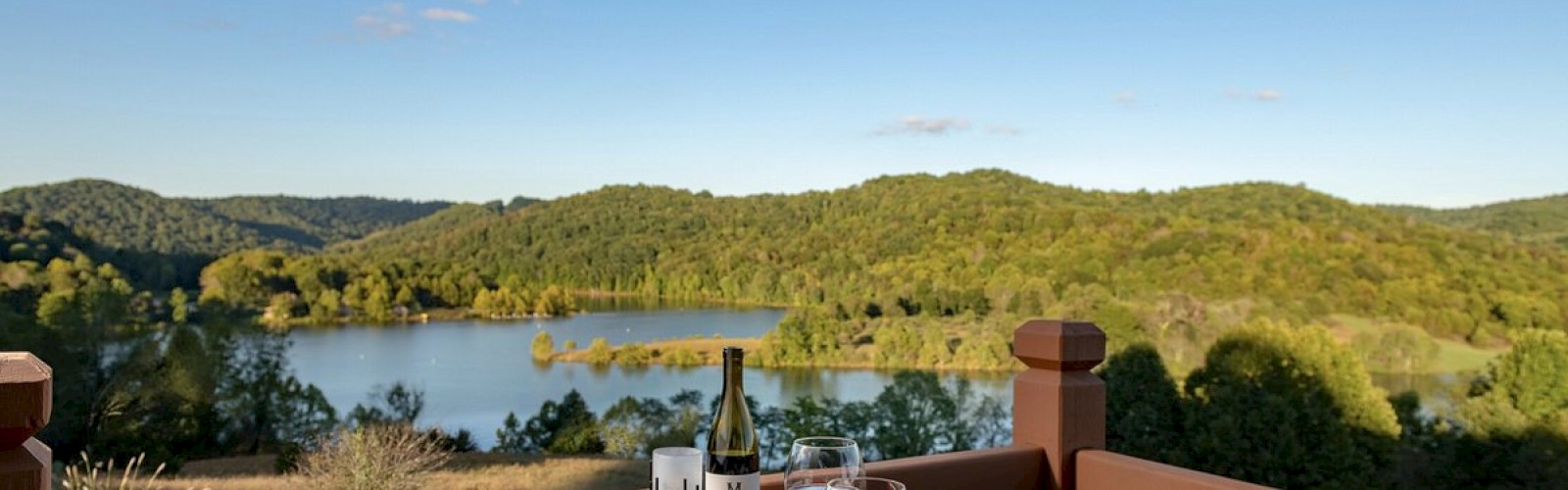 A scenic lakeside dining setup with food and wine on the table.